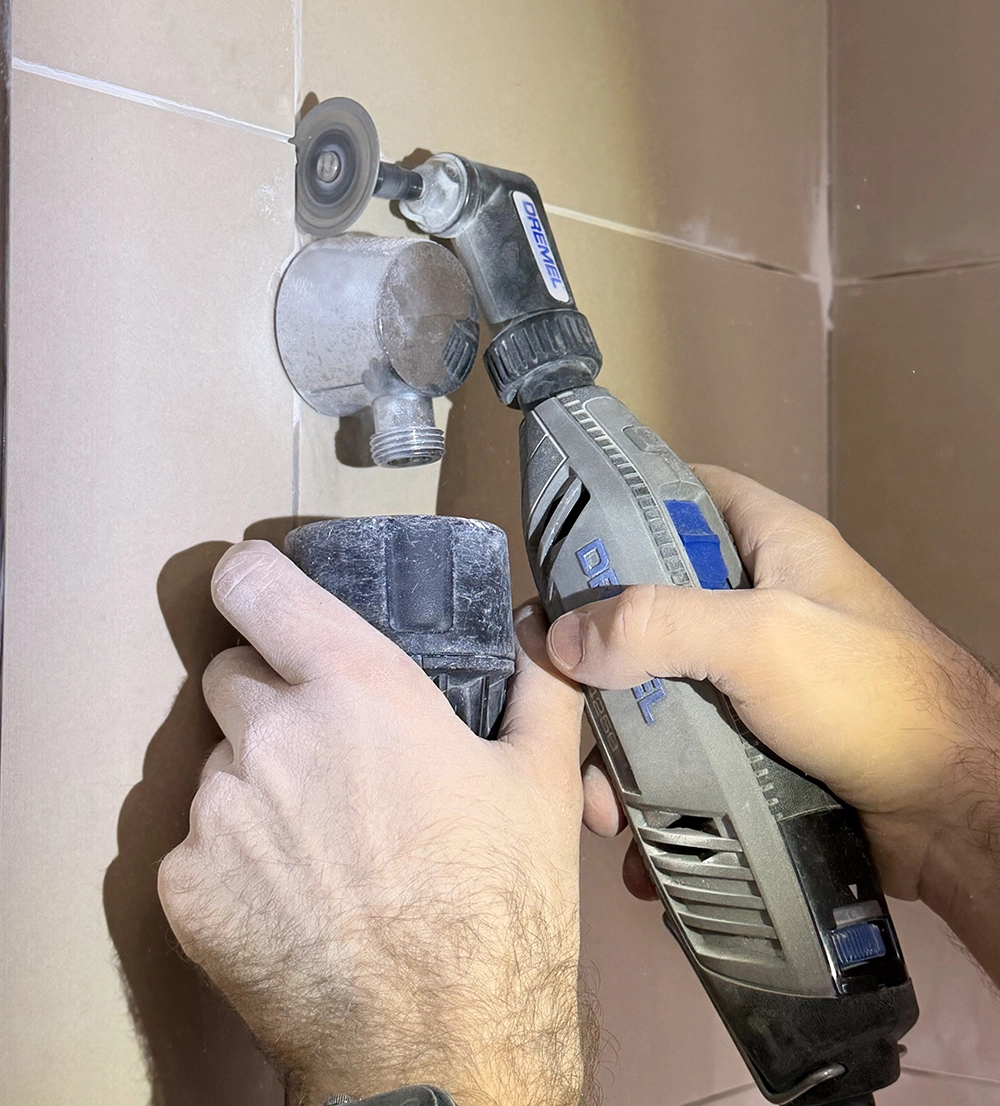 Technician repairing a leaking shower mixer by tightening a gold shower tap on a tiled wall