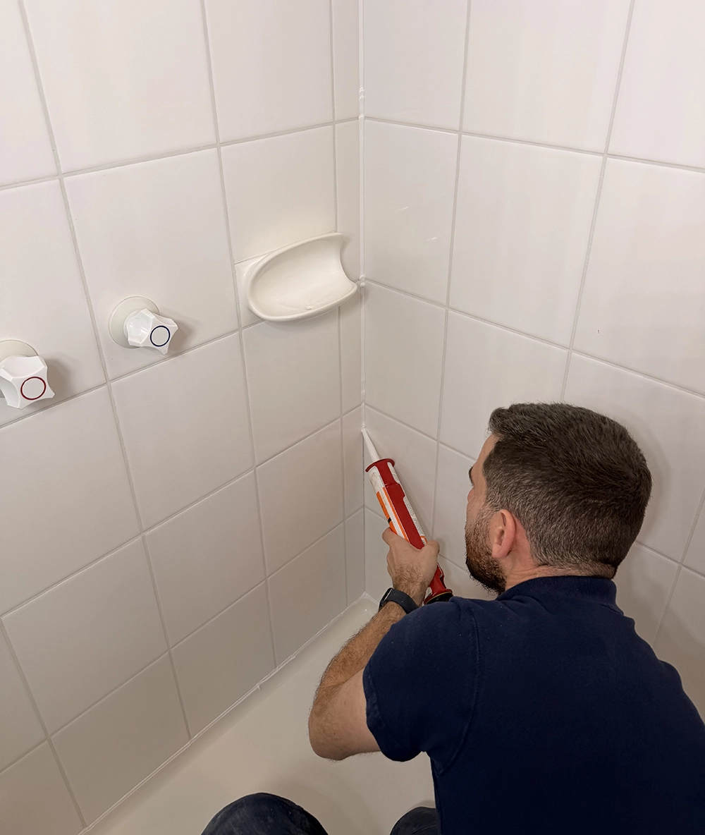 Shiny Shower specialist sealing a shower screen with a caulking gun to repair a leaking shower